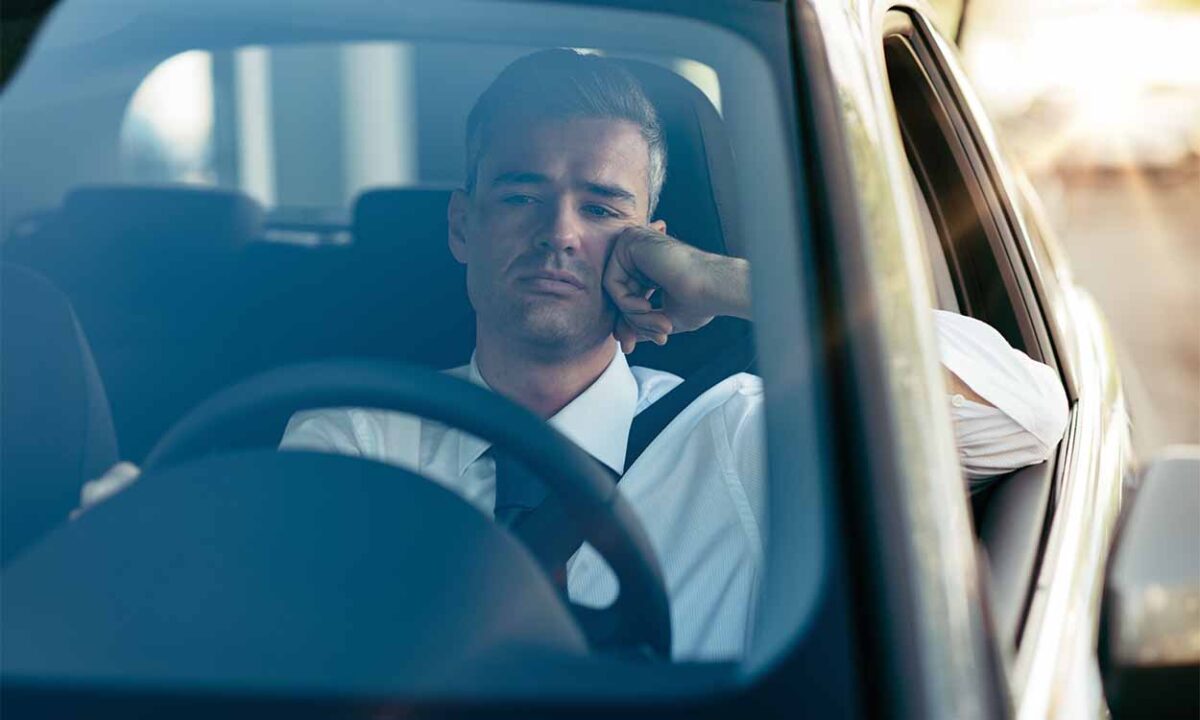 Foto mostra homem sentado em um carro com um semblante triste.