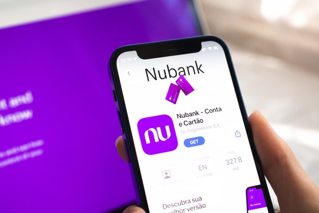 Mão segurando celular que está exibindo tela do app Nubank em loja de aplicativo.