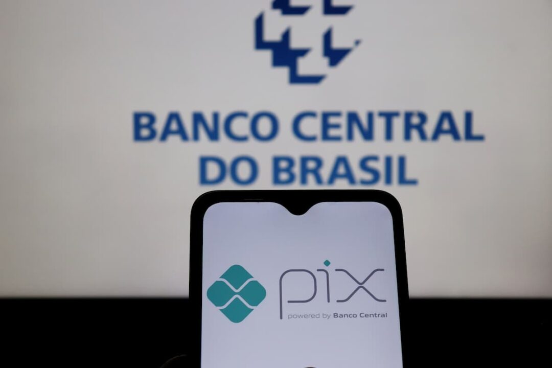 celular com logo do pix, ao fundo uma tela de laptop com logo do Banco Central
