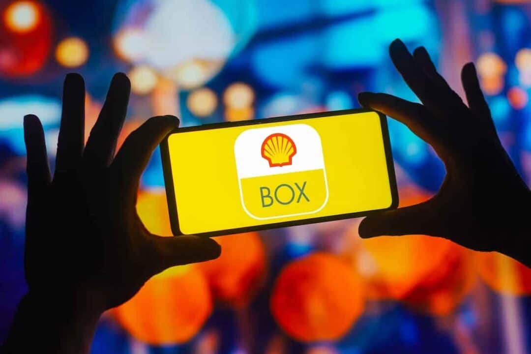 silhueta de mãos segurando um celular com logo da Shell Box em um fundo colorido