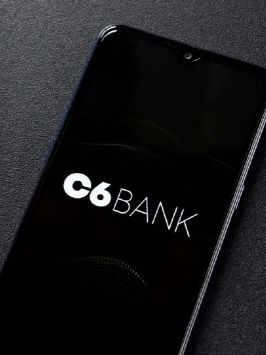 Imagem de um celular com a tela na logo do C6 Bank. Ao lado, uma calculadora fazendo os cálculos referentes a um consórcio
