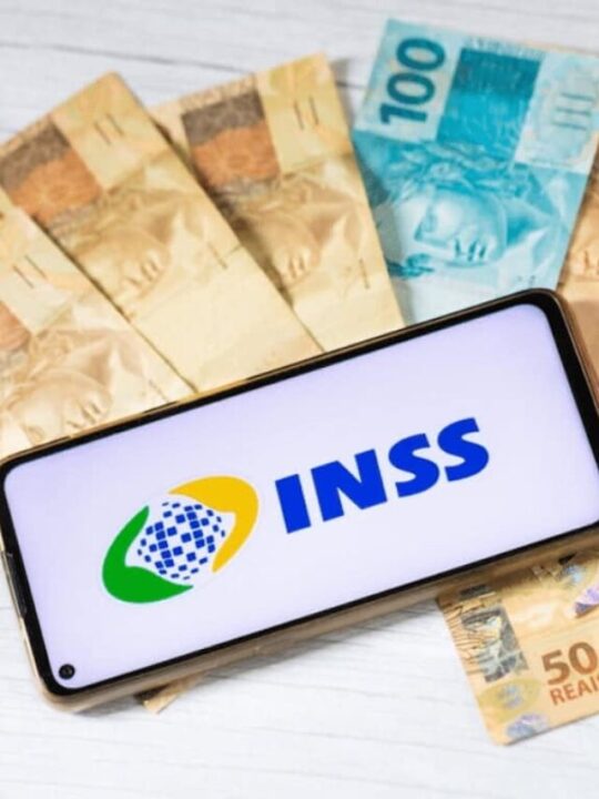 Notas de dinheiro com um cofrinho e o aplicativo do INSS aberto em um celular