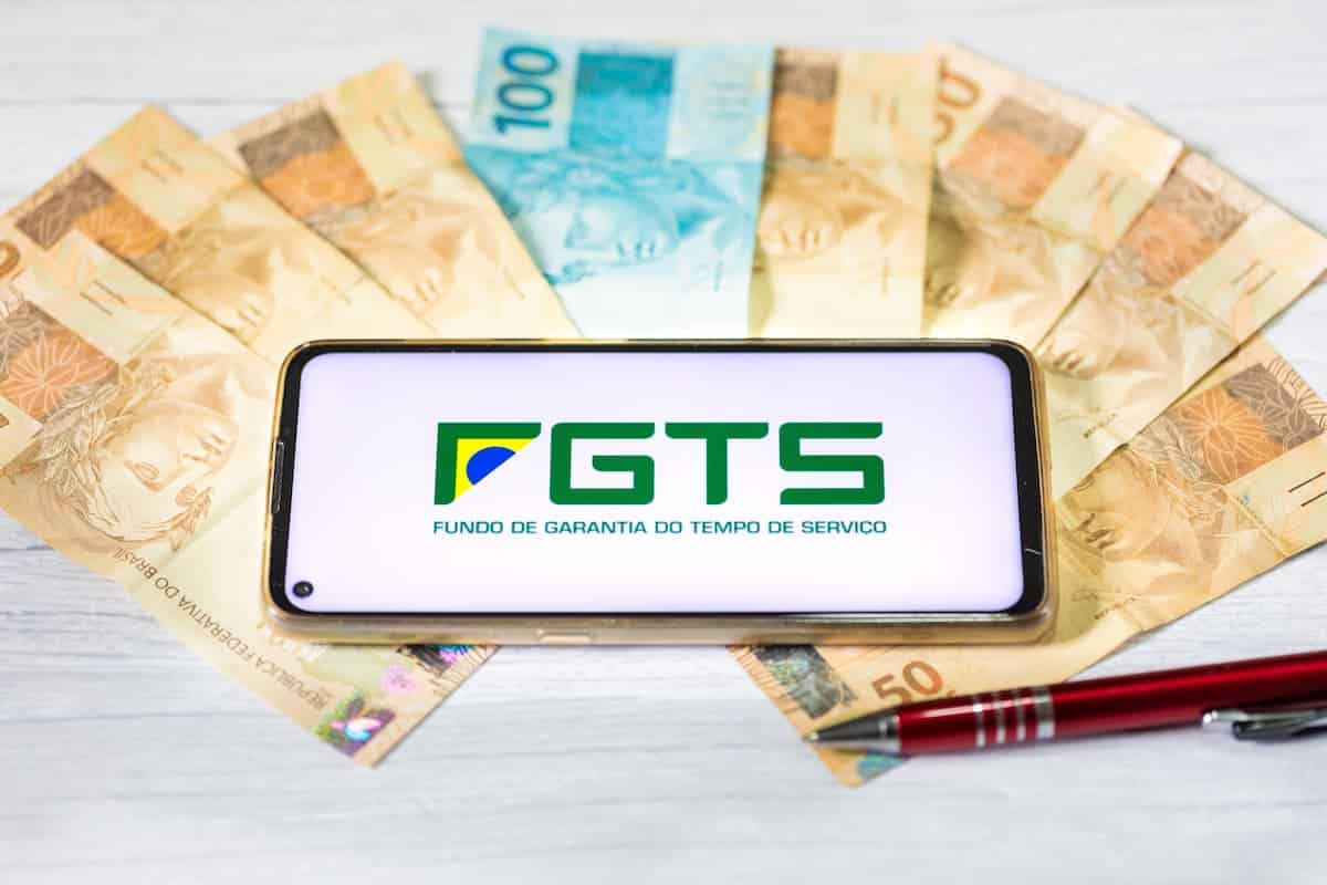 Celular com aplicativo do FGTS sobre diversas notas de dinheiro, simbolizando o saque da Caixa.