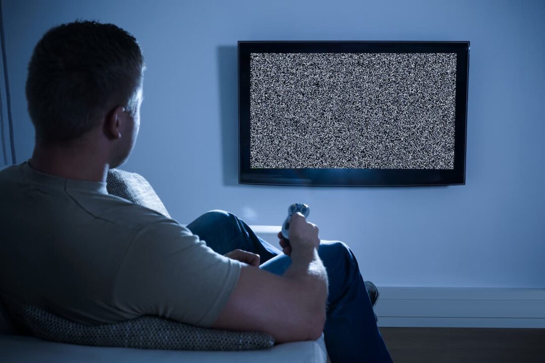 homem com controle em frente a televisor sem sinal