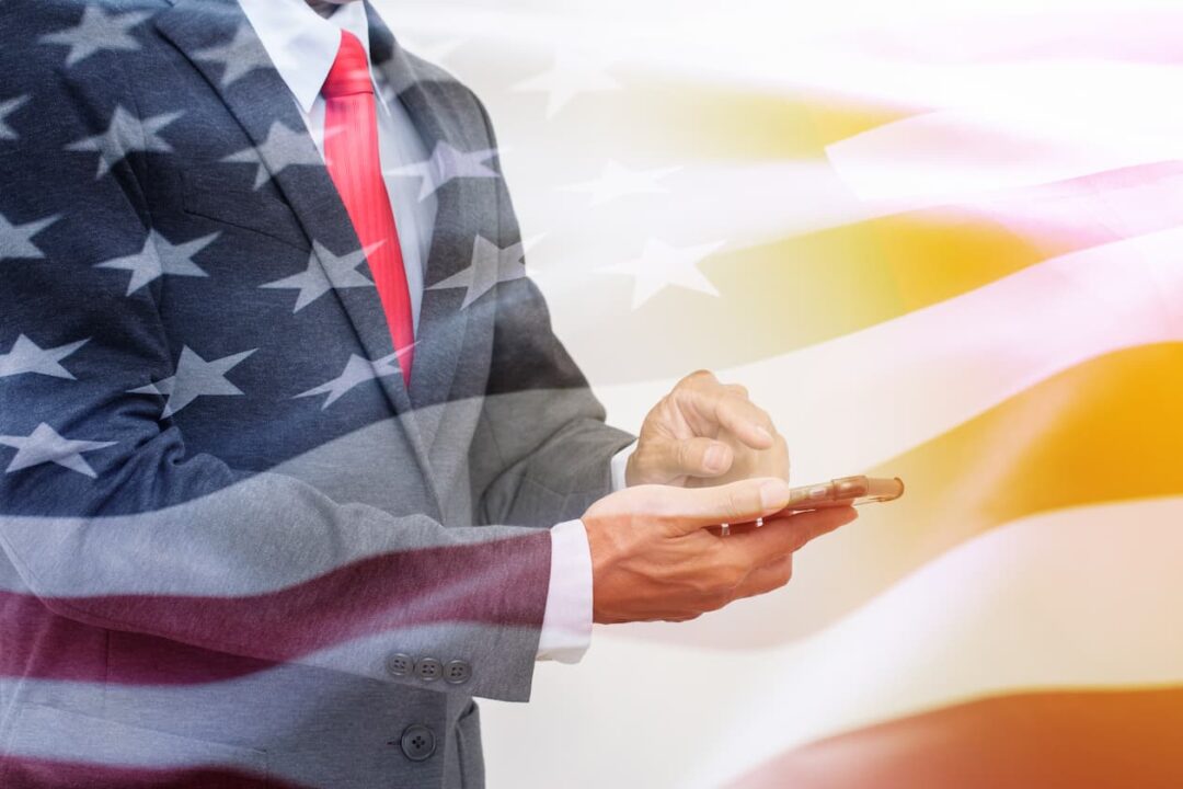 homem engravatado usando celular e bandeira dos Estados Unido sobreposta na imagem