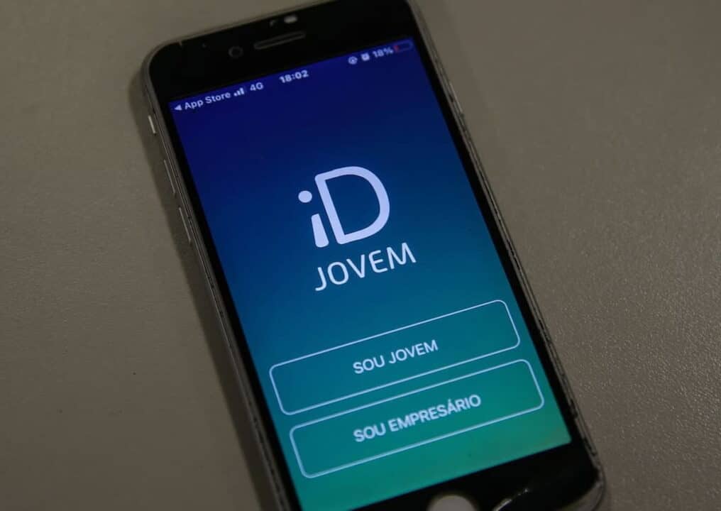 Mão segurando celular que contém imagem do aplicativo ID Jovem