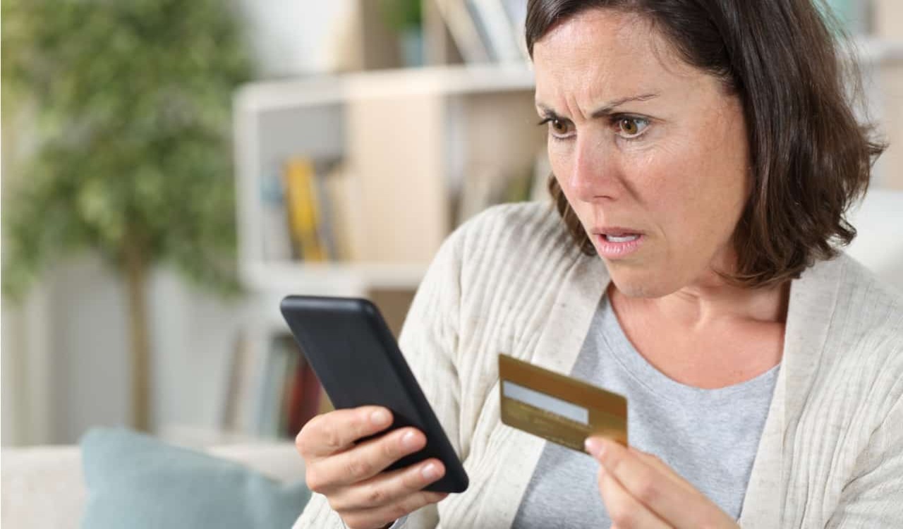 Mulher assustada com cartão de crédito clonado na mão