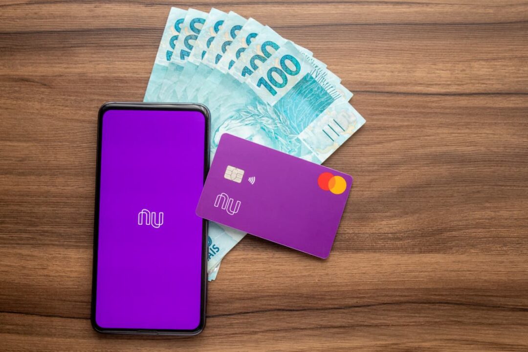 Celular iniciando o aplicativo Nubank, cartão e dinheiro. Simbolizando empréstimo na instituição.