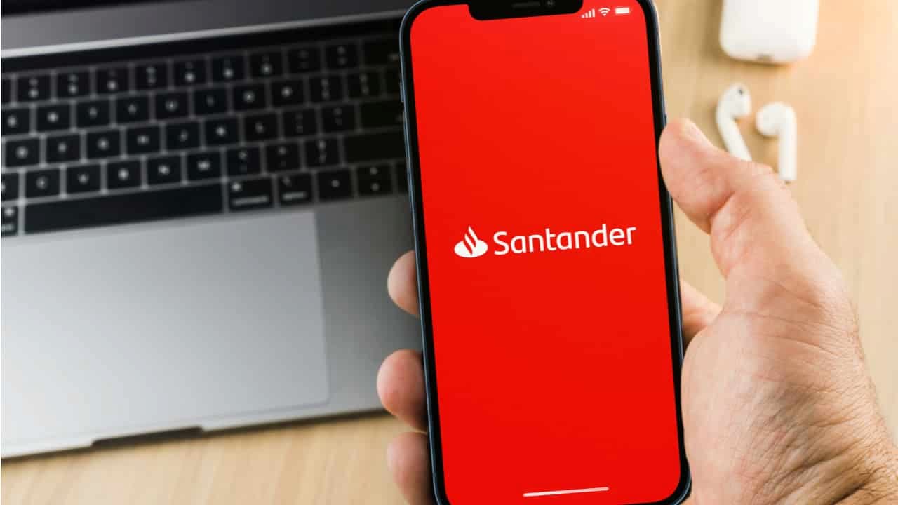 Smartphone com aplicativo Santander aberto. Teclado de notebook ao fundo