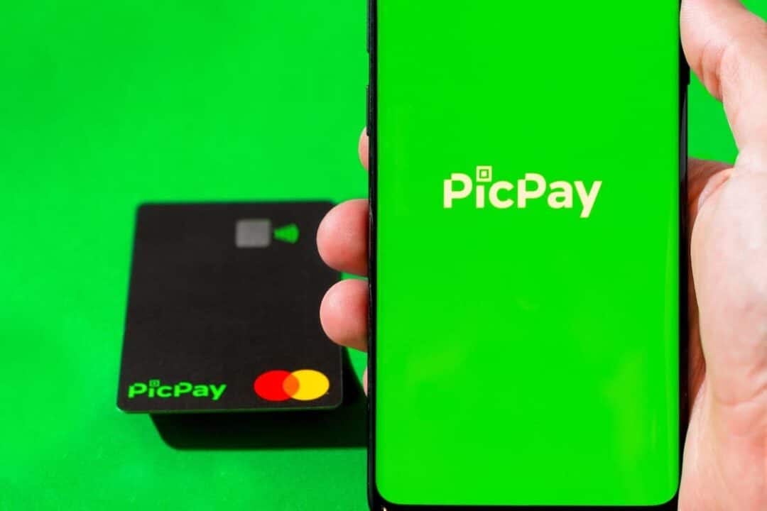 Aplicativo PicPay em celular na mão de uma pessoa, com cartão ao lado