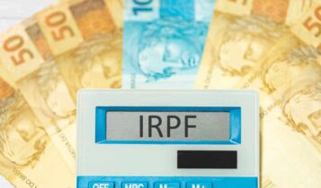Calculadora sobre um leque de notas de 50 e 100 reais com a sigla IRPF (Imposto de Renda sobre a Renda da Pessoa Física) na tela
