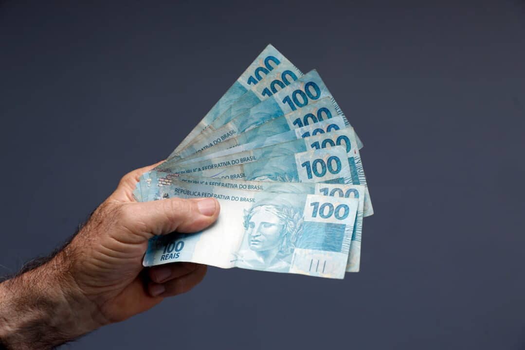 Mão segurando notas de 100 reais