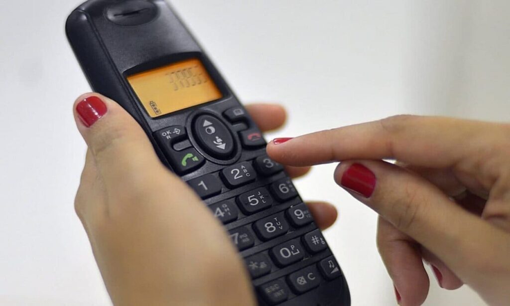 Pessoa discando os números em um aparelho telefônico sem fio
