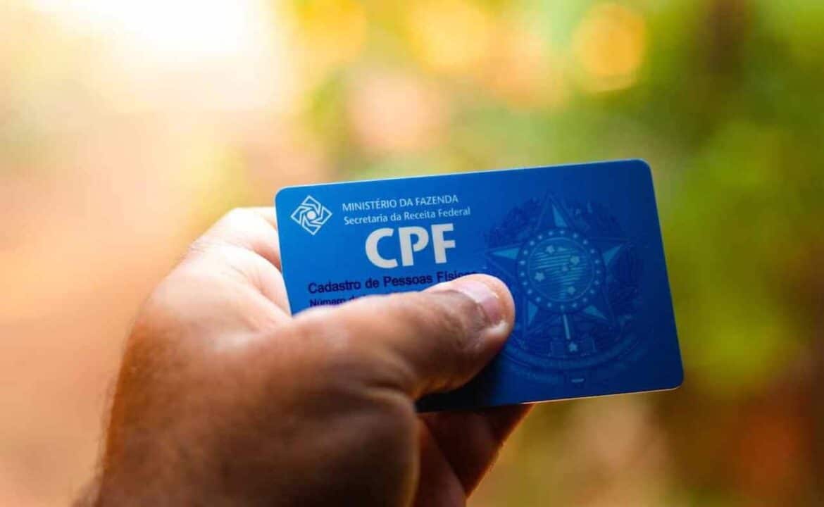 Na imagem, uma mão segurando um CPF com fundo distorcido colorido CPF nova lei