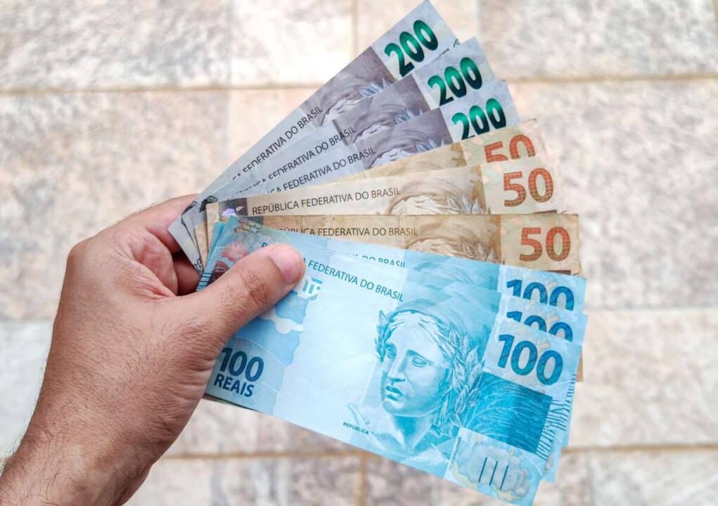 Na imagem, mão segurando cédulas de cem, cinquenta e duzentos reais.