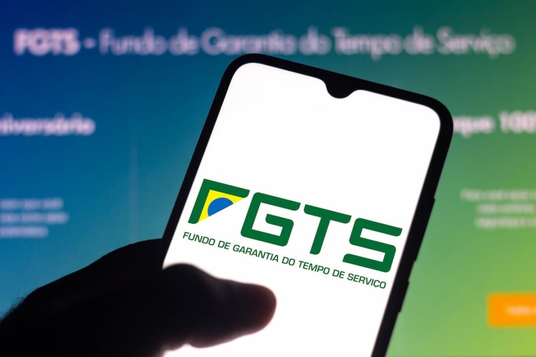 Aplicativo do FGTS em celular de usuário com tela em site do mesmo no plano de fundo.