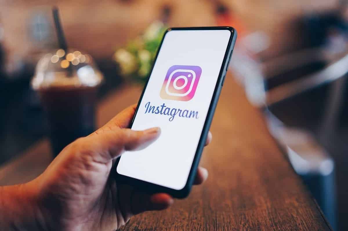 Mão segurando um smartphone com a logo do Instagram, rede social da Meta, na tela.