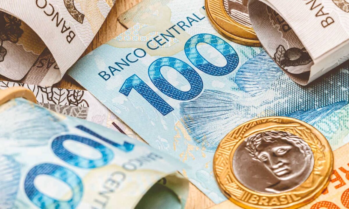 Várias notas de R$ 100 e R$ 200 espalhadas representando um auxílio do governo.