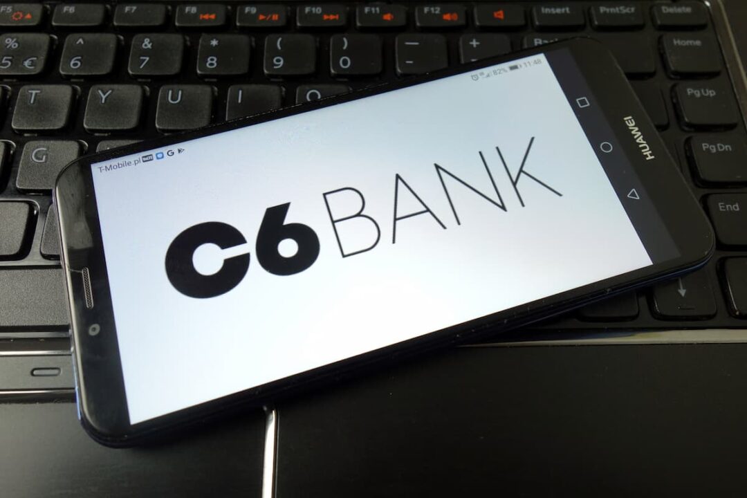 Aplicativo C6 Bank em celular de usuário apoiado sobre notebook