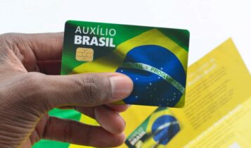 Mão segurando o cartão do Auxílio Brasil