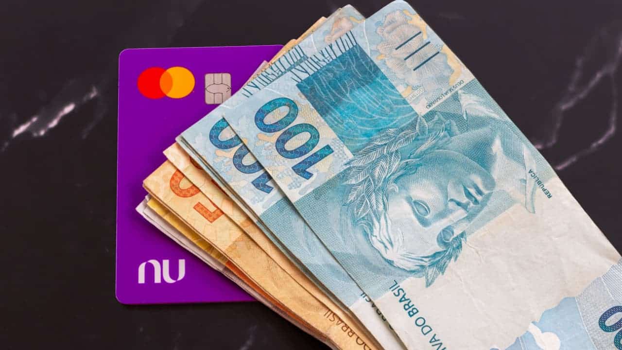 Notas de 100 e 50 reais sobre um cartão do Nubank.