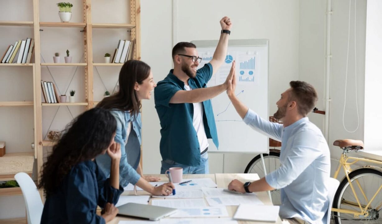 pessoas em uma sala de trabalho conversando e batendo as mãos no alto