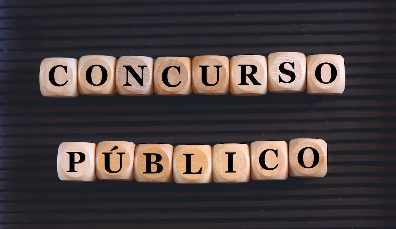 Cubos de madeira com letras do alfabeto formando as palavras "concurso público" sobre uma superfície preta. Concurso do Ministério da Fazenda vagas cnu concurso