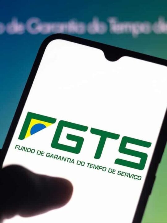 Aplicativo do FGTS em celular de usuário com tela em site do mesmo no plano de fundo.
