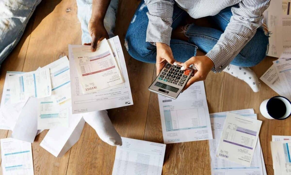 A imagem mostra uma pessoa sentada calculando dívidas.