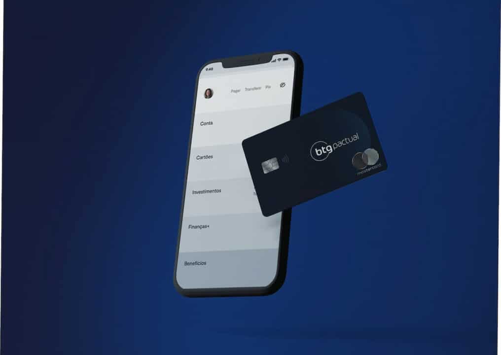 Cartão Black do BTG Pactual com um celular ao fundo e o aplicativo do banco.