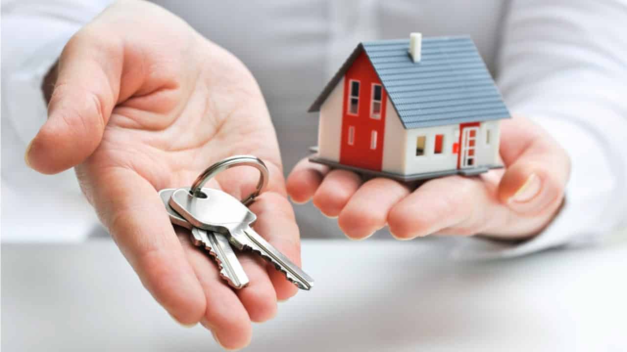Mão estendida segurando uma chave e na outra um modelo miniatura de uma casa de uma cidade cara