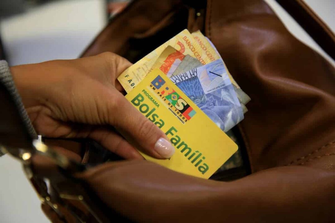 Cartão do Bolsa Família e dinheiro na mão de mulher