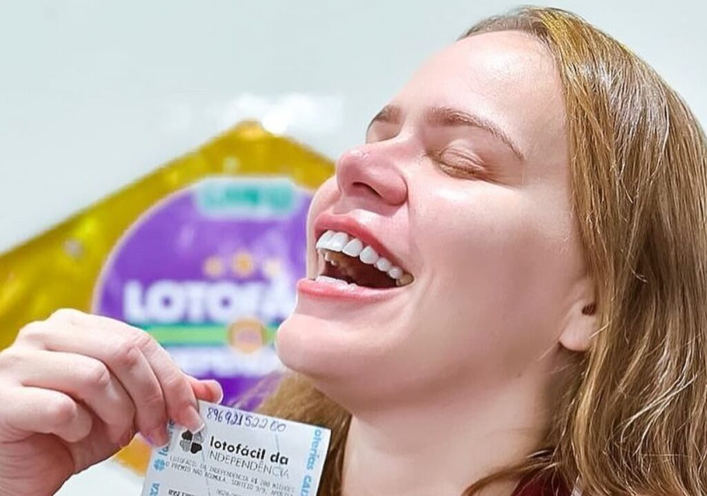 Imagem da ex-bbb Paulinha Leite de perfil segurando um canhoto da lotofácil