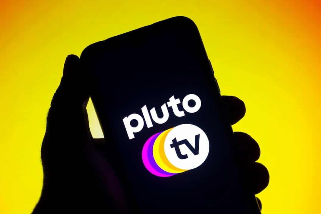 Mão segurando celular que mostra identidade visual da Pluto TV