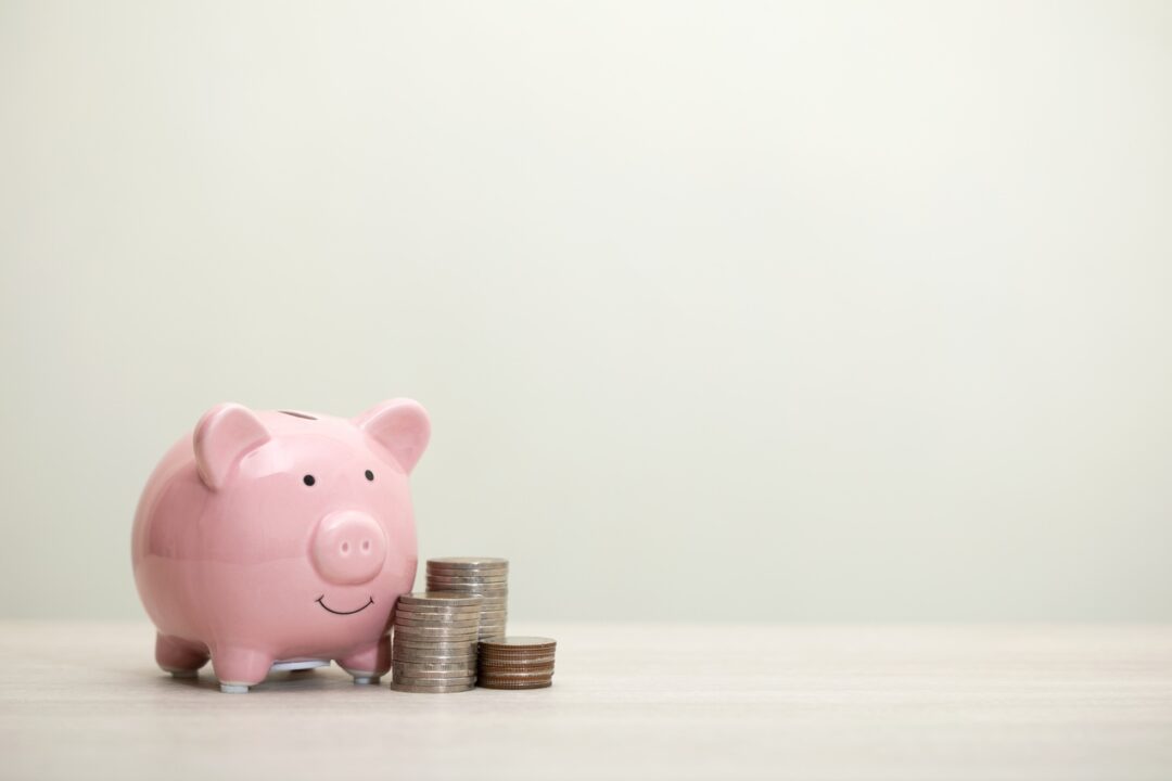 Cofre de porquinho sorrindo com uma pilha de moedas ao lado representando a poupança