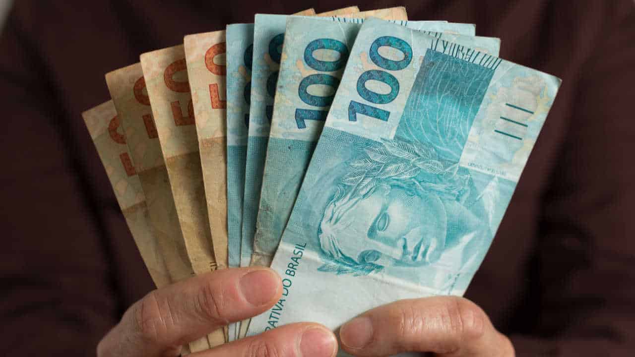 Notas de R$ 50 e R$ 100 na mão, fotografadas em primeiro plano