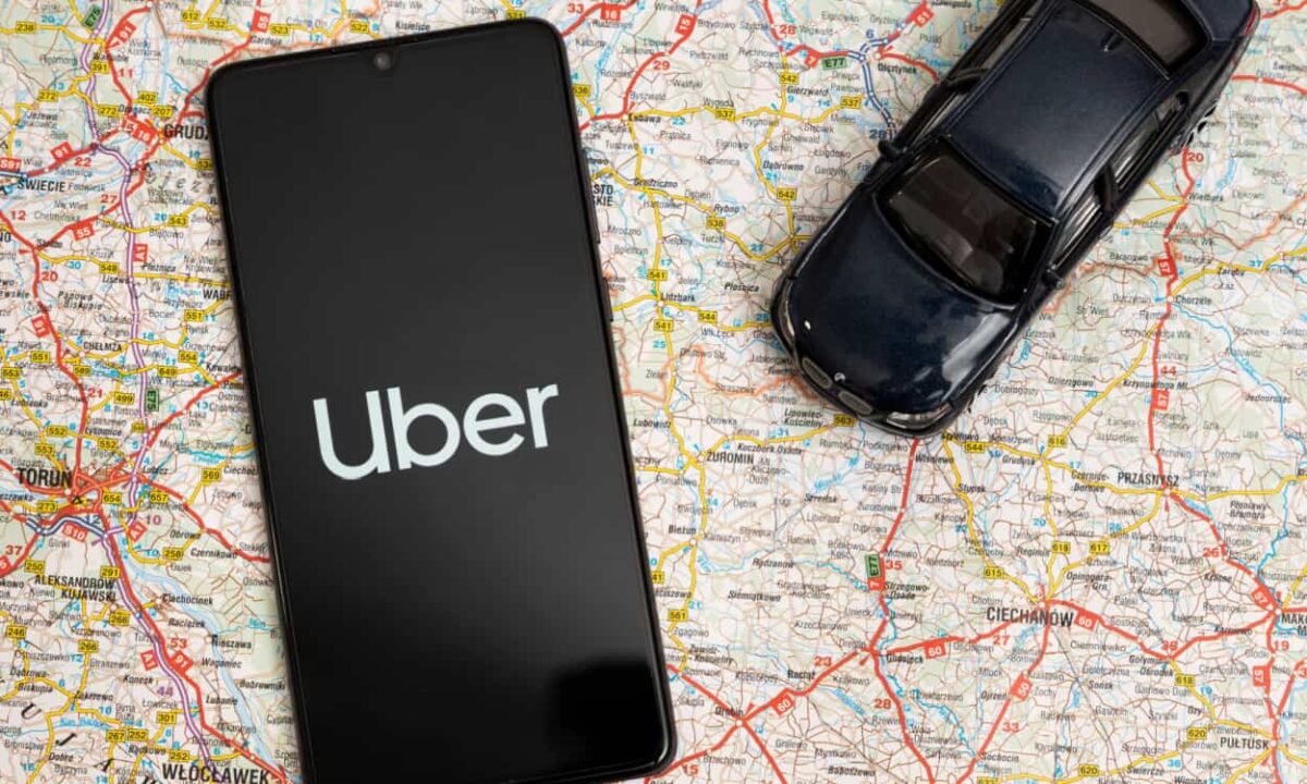 Em cima de um mapa, celular com a logo da Uber e miniatura de um carro preto.