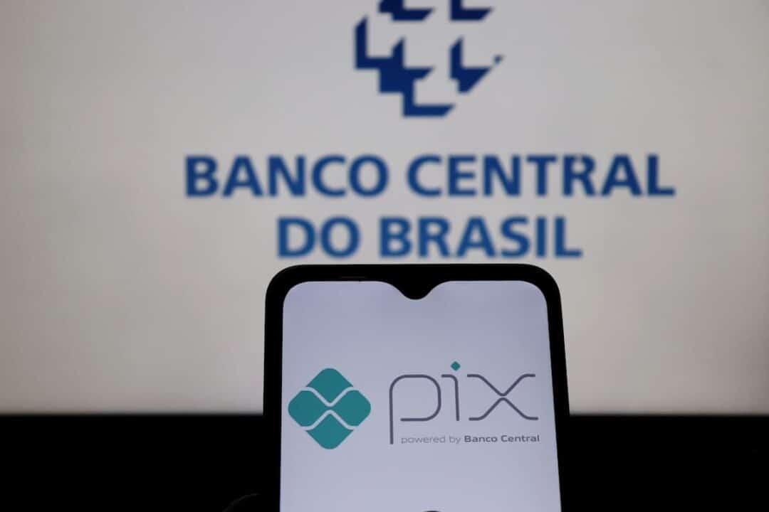 Celular com logo do pix, ao fundo uma tela de laptop com logo do Banco Central.