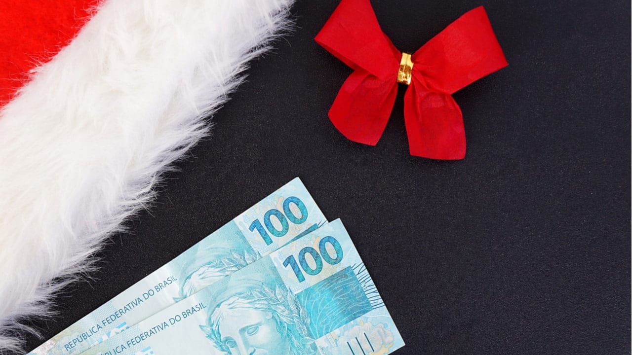 Notas de 100 reais, laço vermelho e gorro de Papai Noel