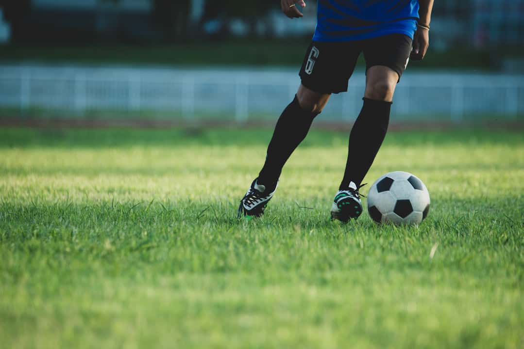 Homem de uniforme de time de futebol chutando uma bola no gramado.