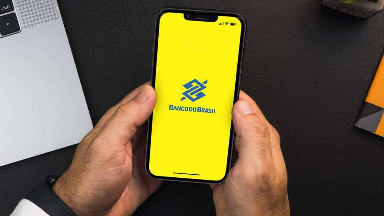 Celular na mão com app do Banco do Brasil aberto na tela inicial