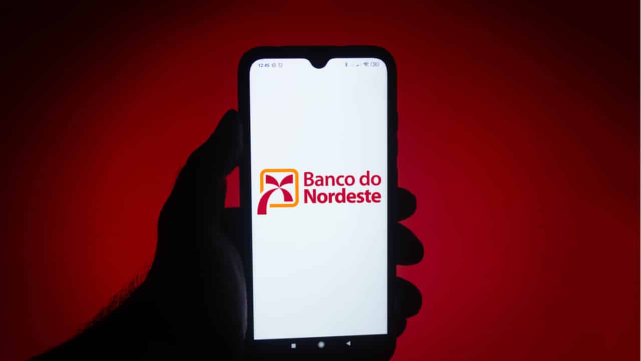Mão segurando celular com logo do Banco do Nordeste