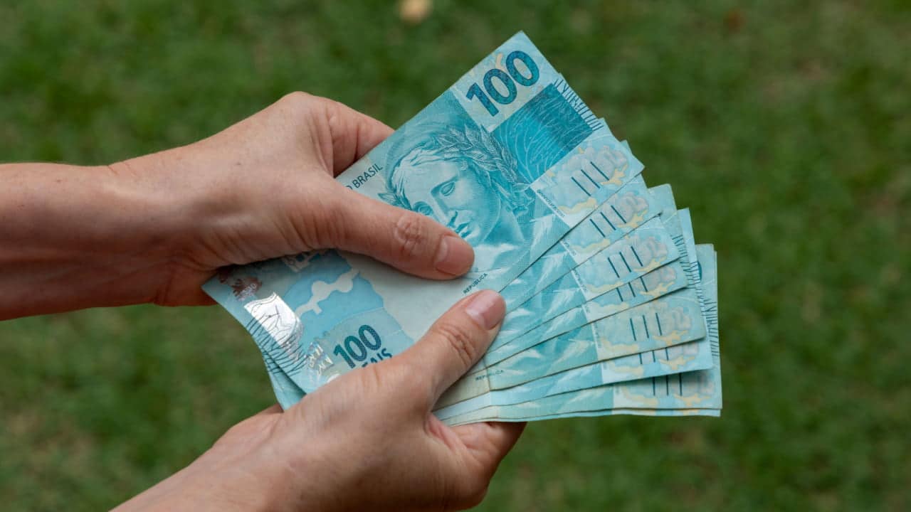 Mão segurando um notas de 100 reais.