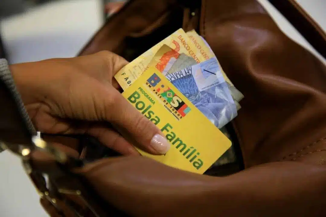 Cartão do Bolsa Família e dinheiro na mão de mulher.