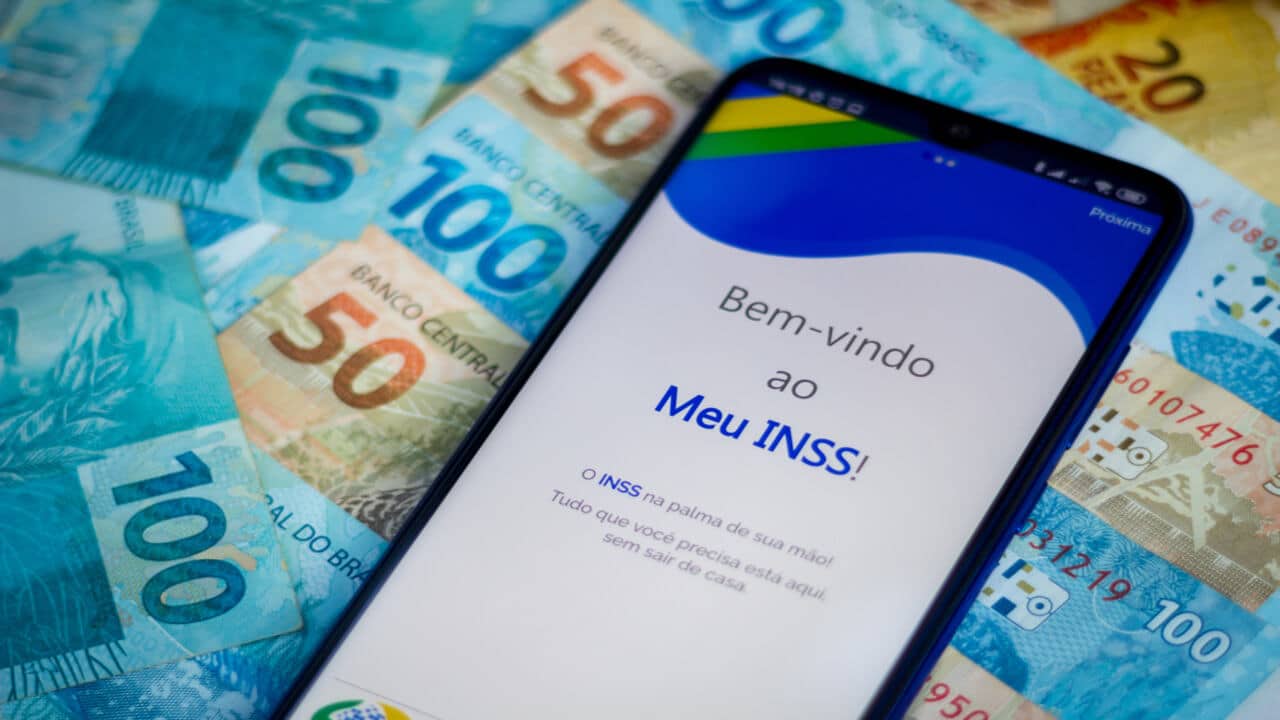 Celular com tela no app Meu INSS e notas de 50 e 100 reais
