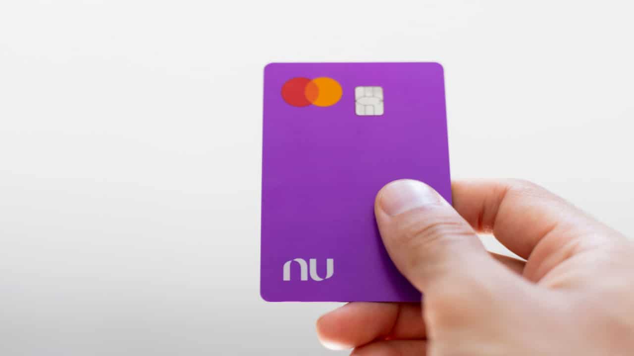 Mão de pessoa branca segurando um cartão de crédito do Nubank