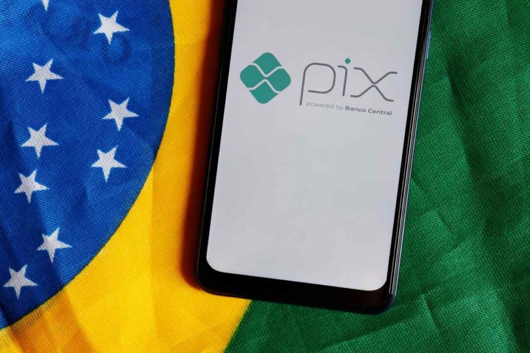 Celular exibindo a ferrameta PIX na tela com a bandeira do Brasil no fundo