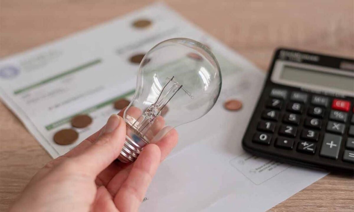 Na imagem, mão segurando uma lâmpada perto de uma conta de luz e uma calculadora.