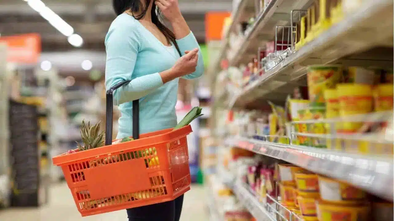 Mulher parada em frente a prateleira de supermercado vendo o desconto de um produto