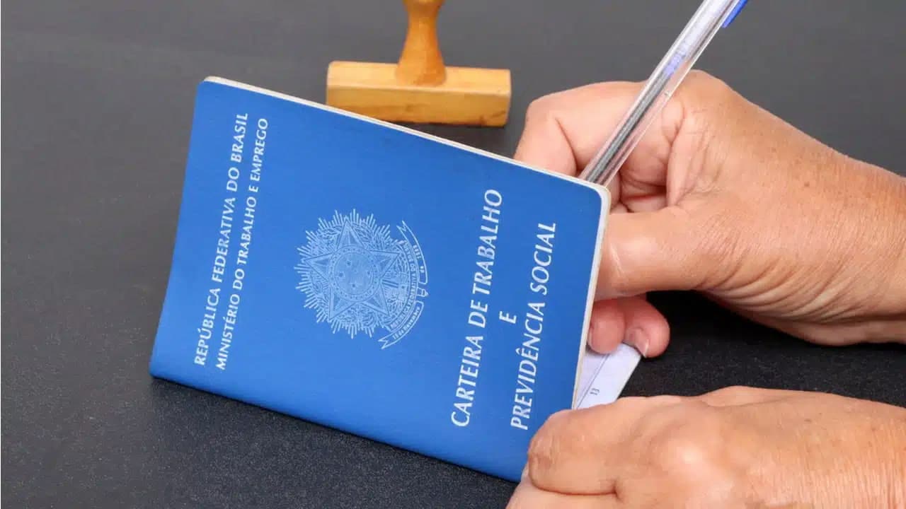 Mão assinando uma carteira de trabalho